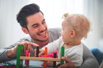 Obraz premium Young dad playing with his little daughter on sofa at home