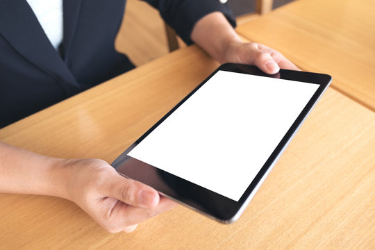 Mockup image of business woman holding black tablet pc with blank white desktop screen on wooden table