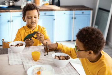 Having fun together. Charming little boys playing with their toy dinosaurs while sitting at the...
