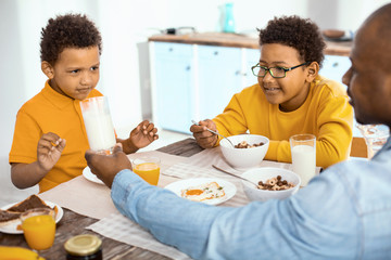 Caring gently. Loving young father holding an empty glass of milk, having helped his son to drink it up during breakfast
