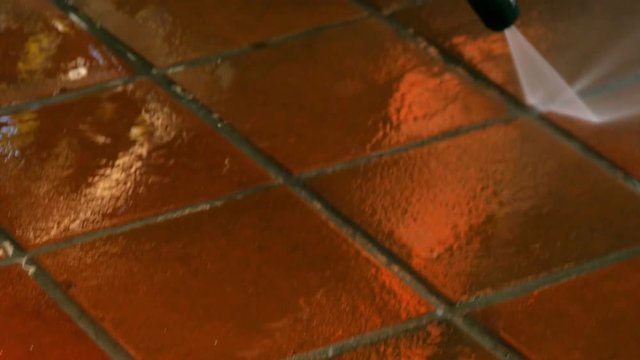 Closeup on cleaning outdoor floor ceramic tiles with high pressure water washer. Water sprinkling and shining in evening sunset. Spring cleaning arround the house.