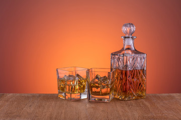 Old fashion glass and carafe with the alcohol, whisky drink on warm, dark orange background and wood
