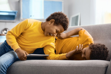 Fototapeta premium Favorite pastime. Upbeat little brothers lying on the sofa and tickling each other, having fun while one of the boys holding a tablet