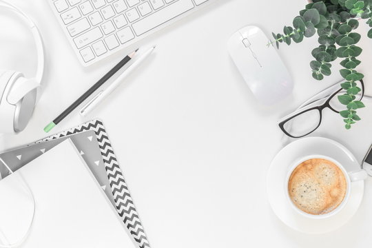 Modern White Office Desk Table With Laptop Computer, Notepad, Plant, Headphones And Cup Of Coffee. Flat Lay, Top View, Copy Space 