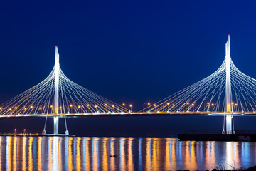 Cable-stayed bridge connects the roads of Western high-speed diameter in St. Petersburg, Russia. Night lighting of bridge is reflected in water of Peter's fairway. Modern industrial road structures