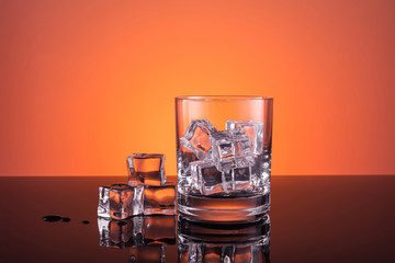 Empty glass with ice prepared for the drink on warm dark orange background