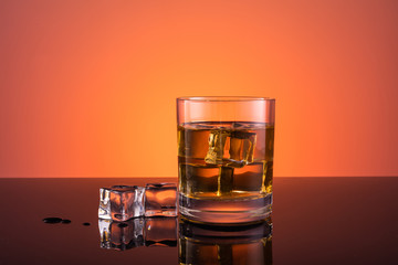 Whisky alcohol in glass with ice, drink on warm dark orange background