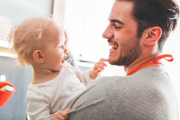 Cute portrait of young handsome father hugging his toddler child daughter in the kitchen at home