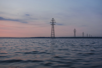 Obraz premium Power lines against a beautiful sunset on the water. The country's industry is a source of heat and light