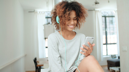 Fototapeta premium Beautiful young afro american woman texting on mobile phone at home.