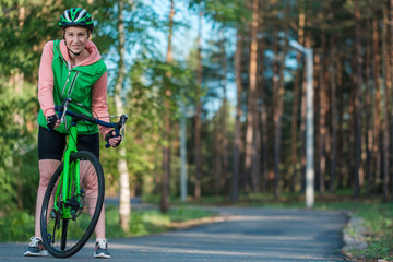 Beautiful smiling blond girl is riding the bicycle in the park. Green vest, bicycle and green helmet. Doing sports.