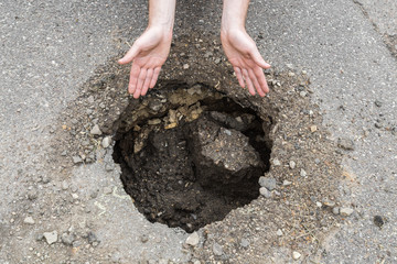 Driver's hands showing to the big, deep hole on the asphalt road. Dangerous, bad automobile driveway. Damaged surface.