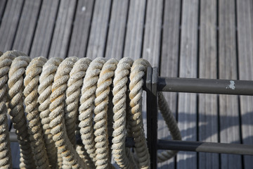 Rigging ropes on board an old wooden sailing ship neatly stored on a metal frame in a close up view with wood decking background