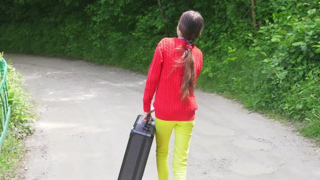 girl, walks through the woods with a heavy black suitcase. 4k, slow-motion shooting, steadicam shot.