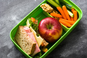 Healthy school lunch box: Sandwich, vegetables ,fruit and juice on black stone. 