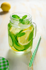 Detox water infused with sliced lemon, cucumber and sprigs of mint on wooden background.