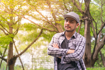Portrait Handsome man : Good looking young man. He has a beard and wears a hat. He has an interesting smile. Looking for someone. Behind him, full of green trees. Copy space.