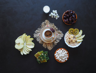 Breakfast with muesli on black background. Black coffee with Turkish sweets, muesli, dates and milk. Sweet food for Ramadan.