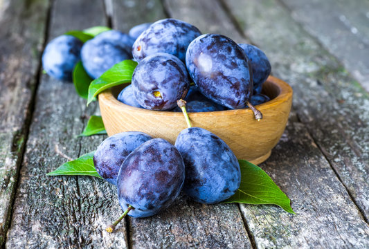 Fresh plums on wooden table background. Half of blue plum fruit. Many beautiful plums with leaves.Harvest. Autumn harvest.