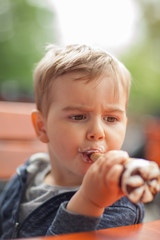 Little boy eating an ice outside in the park at a table, summerly mood 