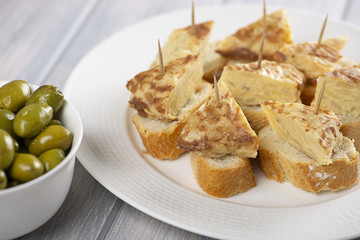 Plate with omelette caps next to bowl with olives on wooden table. Typical spanish food.