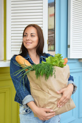 Girl in a jeans jacket is holding a paper bag with food in her hands. The woman stinted in the supermarket. Leaves of lettuce.