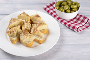 Plate with omelette caps next to bowl with olives on wooden table. Typical spanish food.