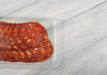 Chorizo made with pork in plastic container on wooden table. Copy space.