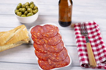 Omelet sandwich with potatoes next to bowl with olives and a beer on wooden table. Typical spanish food.