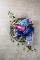 Naturally organic summer sweets, homemade blue and violet ice cream popsicles with butterfly pea flower tea, grey concrete background copy space