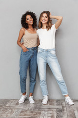 Full length portrait of two smiling young women - obrazy, fototapety, plakaty