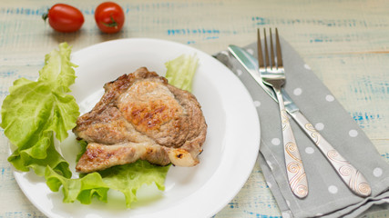 A piece of fried meat on a white plate on a light wooden background.