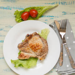 A piece of fried meat on a white plate on a light wooden background.