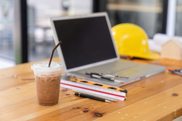 Side view of Iced coffee and a laptop with engineer equipment on a wood table.