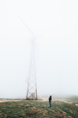 One man looks at huge wind farms, covered with fog, high in the mountains