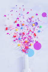 Bottle with bursting confetti flat lay on a white background, party concept with copy space