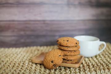 white mug and homemade oatmeal cookies folded in a pile on wooden plate and wooden background
