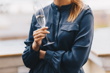 Unrecognizable young female model in elegant dark blue blouse, holds glass of sparkle champagne, has corporative party with colleagues, celebrate successfuly organized meeting with business people