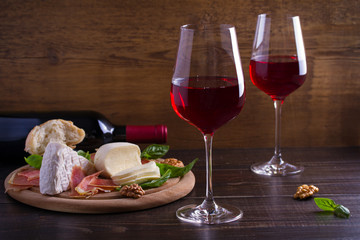 Glasses and bottle of wine with cheese, bread, nuts and jamon or prosciutto on dark wooden background. Wine and food concept