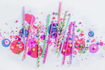 Colorful cocktail straws header with confetti and hard candies. Birthday or party greeting card flat lay with copy space.