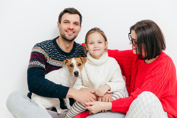 Studio shot of happy family of three family members and dog, embrace and smile happily, have good relationships, isolated on white background. Beautiful small kid with her parents and favourite pet