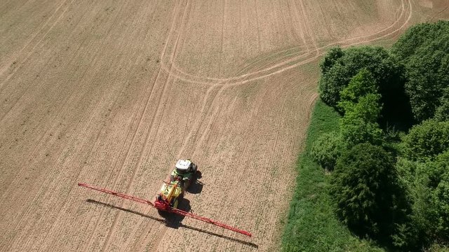 tractor in early spring spraying farmland field with crop sprouts, aerial view