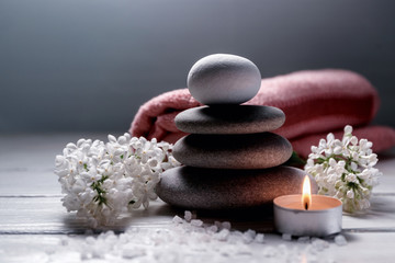 Spa still life with stack of stones,burning candle, sea salt, towel and white flowers on white wooden table