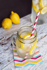 Ice cold fresh lemonade with cut up lemons on a bright wooden background with colorful accessories