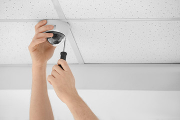 Technician installing CCTV camera on ceiling indoors, closeup