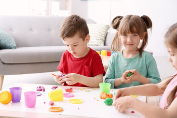 Obraz na płótnie Canvas Cute little children using play dough at table indoors