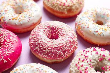 Delicious glazed doughnuts with sprinkles on color background