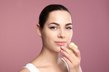 Young woman applying balm on her lips against color background