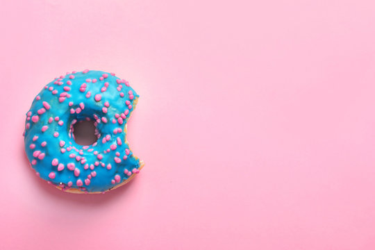 Delicious bitten doughnut with sprinkles on color background, top view
