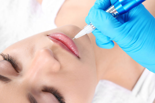 Young woman getting permanent makeup on lips in beautician salon, closeup